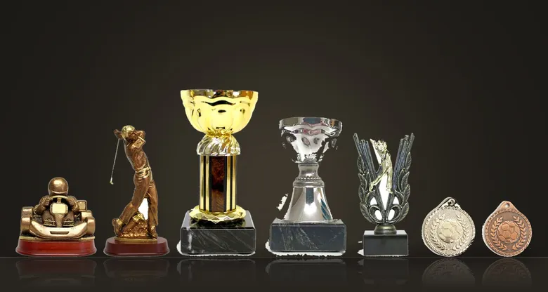 En kartingstatyett, en golfstatyett, pokaler och medaljer ur sortimentet på ett mörkt bord