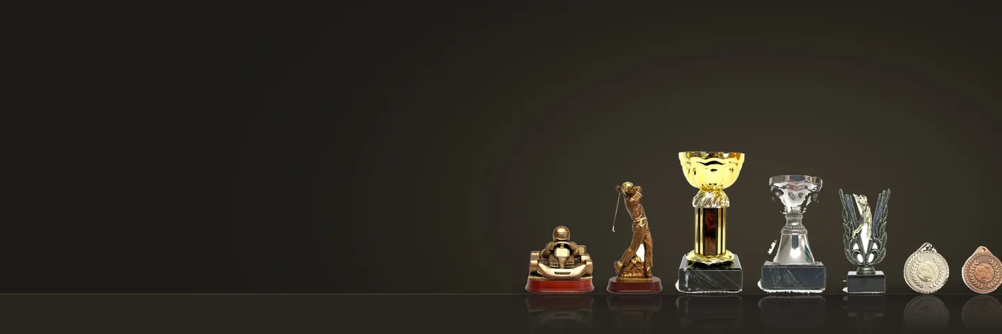 En kartingstatyett, en golfstatyett, pokaler och medaljer ur sortimentet på ett mörkt bord
